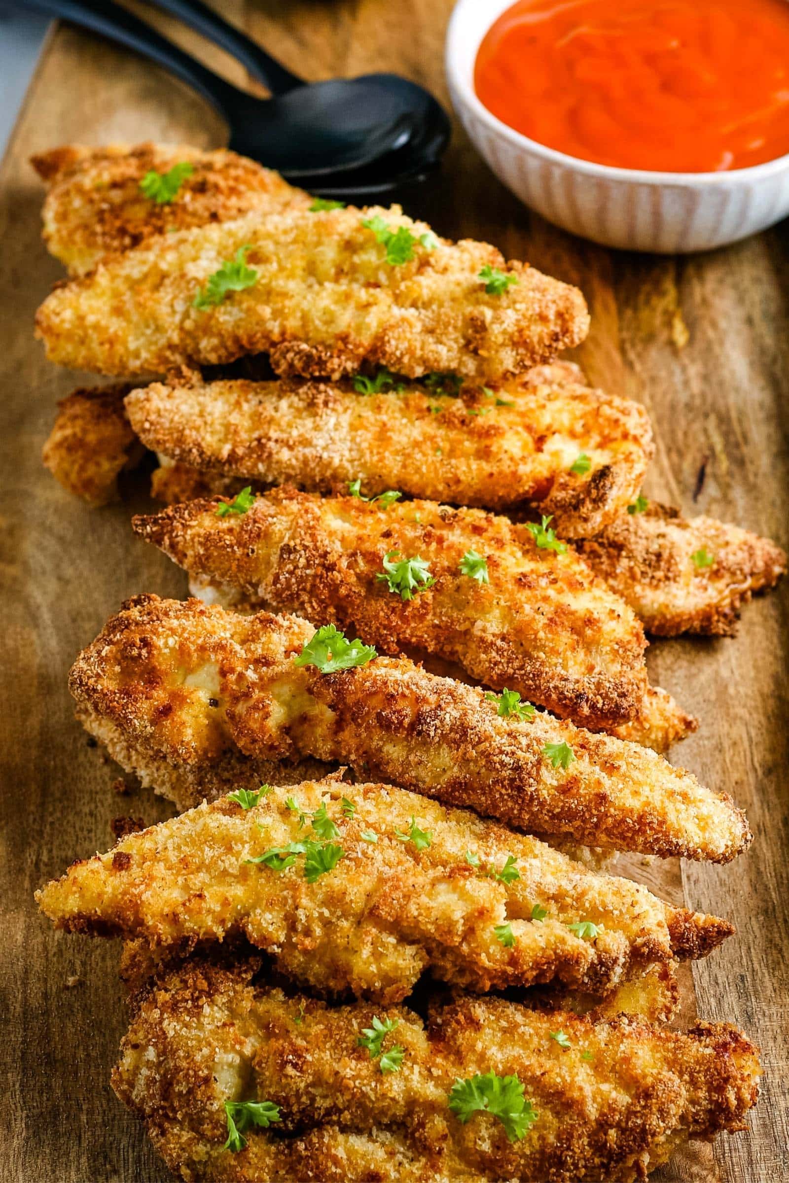 crispy air fried chicken tenders on a wood cutting board with dipping sauce in the background