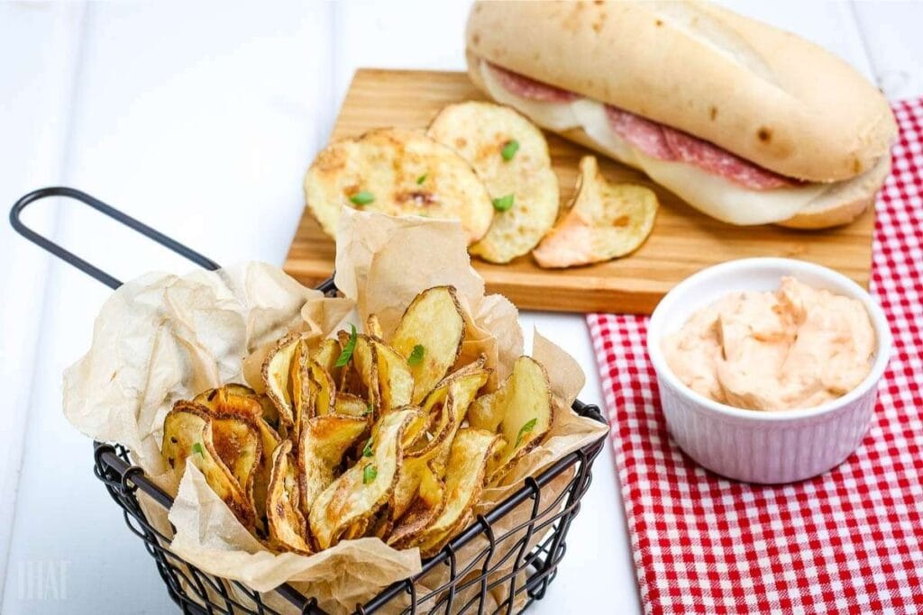 close up of air fryer potato chips in a basket and on a board next to a sandwich