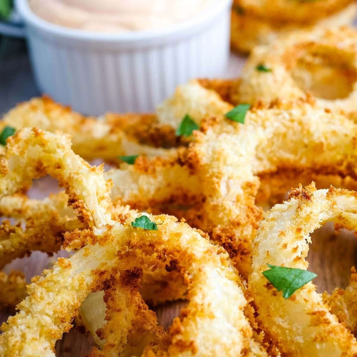 close up of onion rings fresh out of the air fryer with sauce in the background