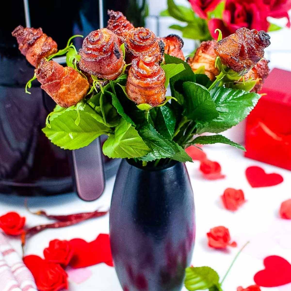 side view of bacon roses in a black vase next to rose petals