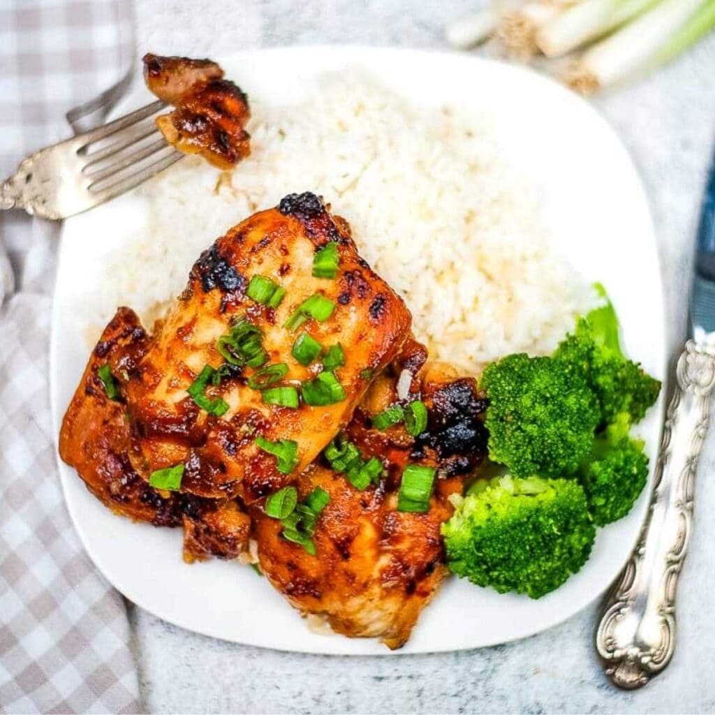 two pieces of Air Fryer Huli Huli Chicken on a plate with broccoli and white rice next to fork and knife