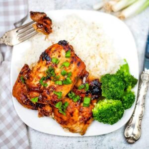 two pieces of Air Fryer Huli Huli Chicken on a plate with broccoli and white rice next to fork and knife