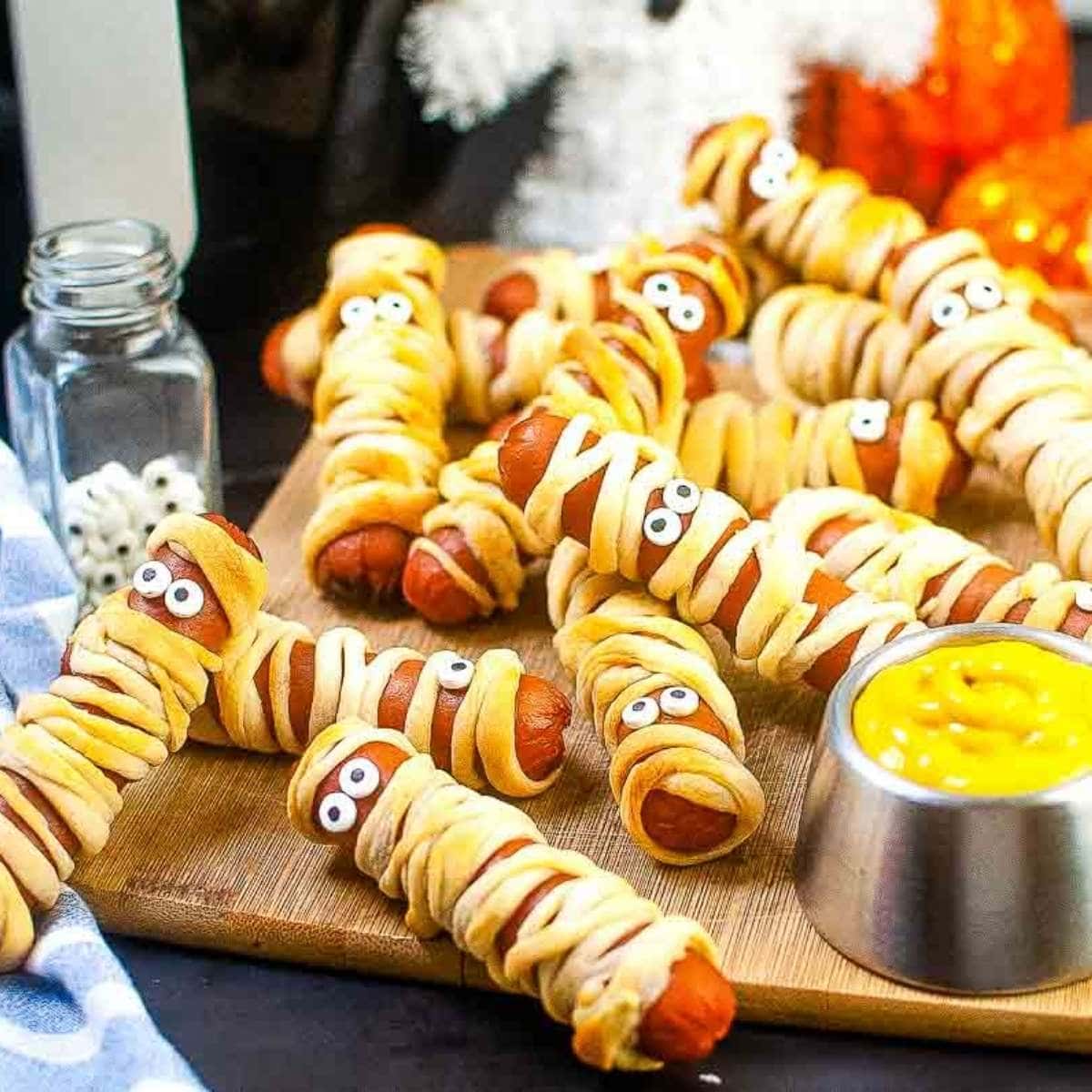 close up of air fryer mummy dogs with a ramekin of mustard on a wooden cutting board.